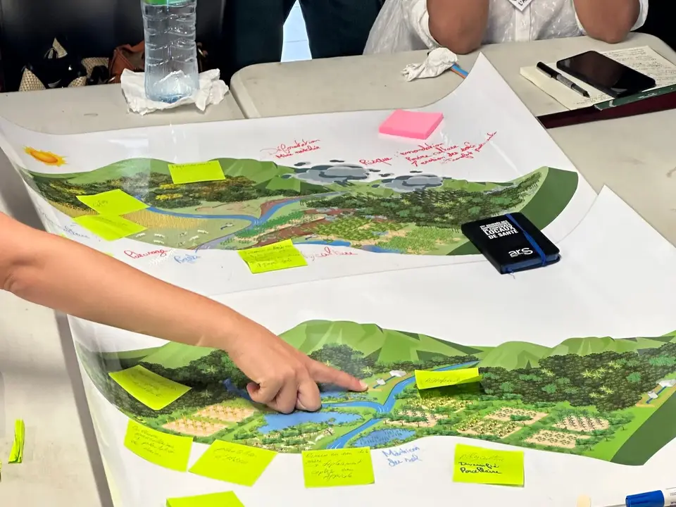 Une main désigne un point sur une carte de paysage annotée de post-its lors d'un atelier de diagnostic partagé