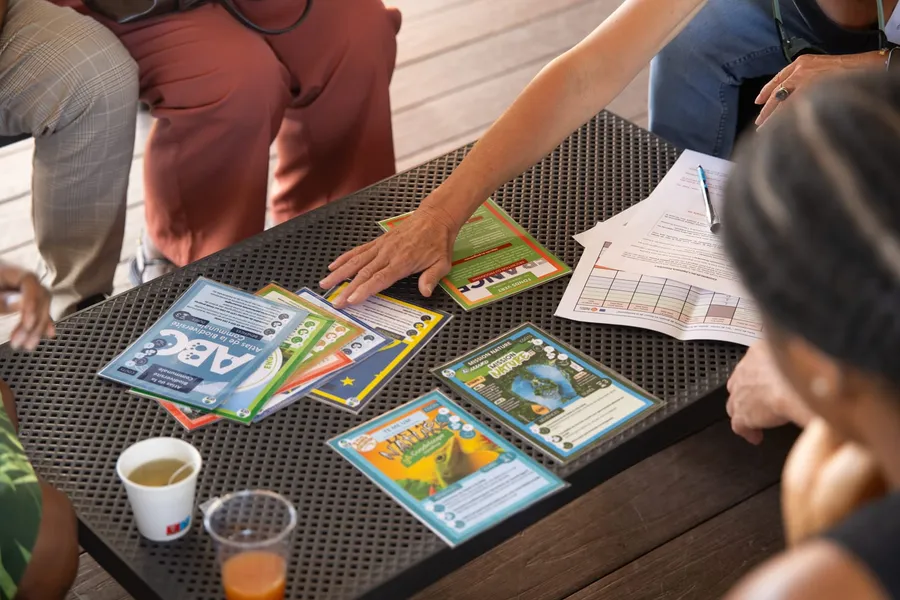 Mains manipulant des cartes présentant les dispositifs de financement LIFE, Fonds Vert, Mission Nature et Atlas de la biodiversité communale lors d'un atelier